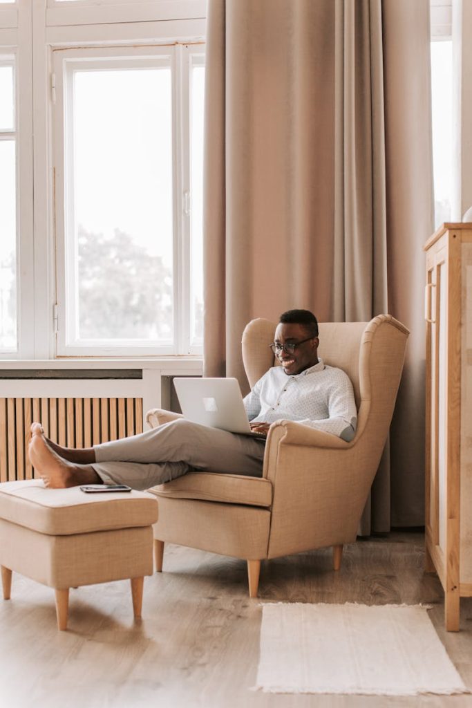 Man sitting in a comfortable chair, working remotely on a laptop in a bright, cozy home setting.